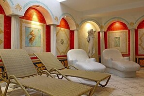 A room with three wicker lounge chairs, a statue, and red-framed artwork on the walls.