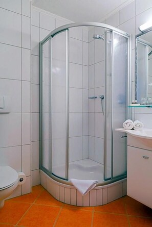 A bathroom with a glass-enclosed shower, a toilet, and a sink with a mirror.