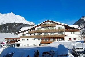 A multi-story hotel with balconies, a ski resort in the background, and snow-covered surroundings.
