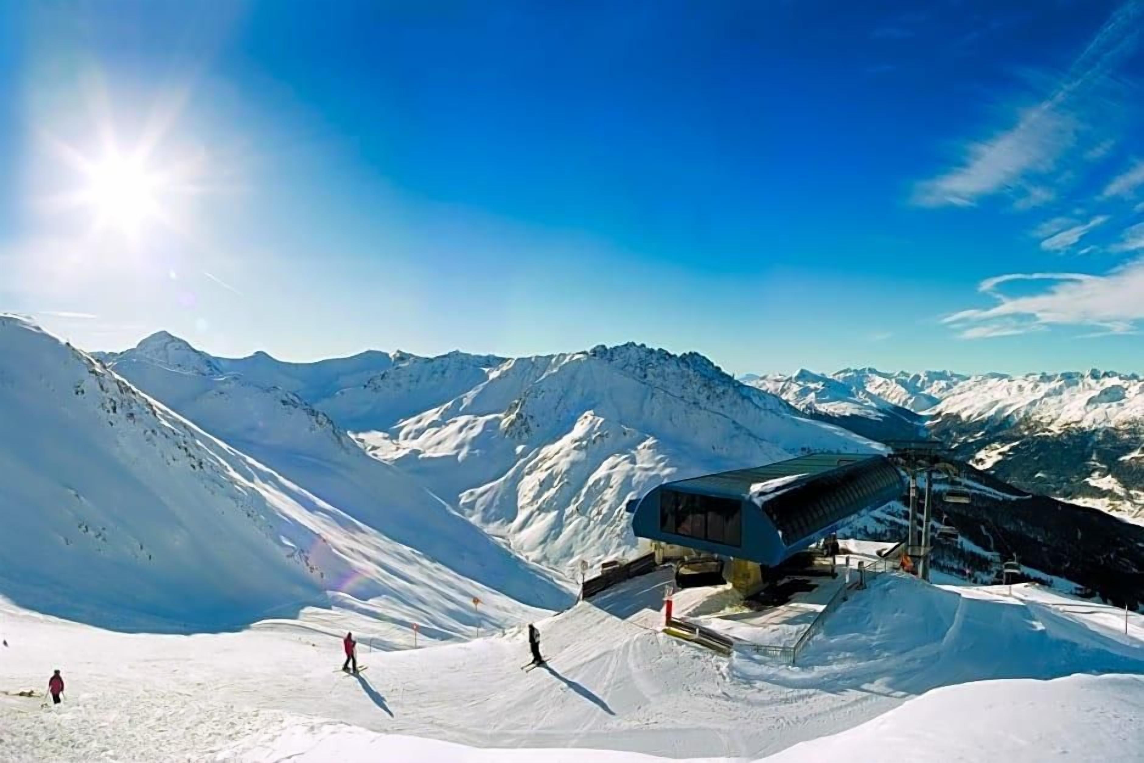 Un paysage de montagne enneigé, avec un télésiège et un bâtiment doté d’un toit en pente.
