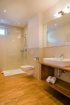 A modern bathroom with a glass-enclosed shower, a white toilet, and a wooden vanity with a sink.