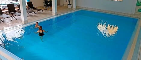 An indoor swimming pool with clear water, surrounded by lounge chairs and potted plants.