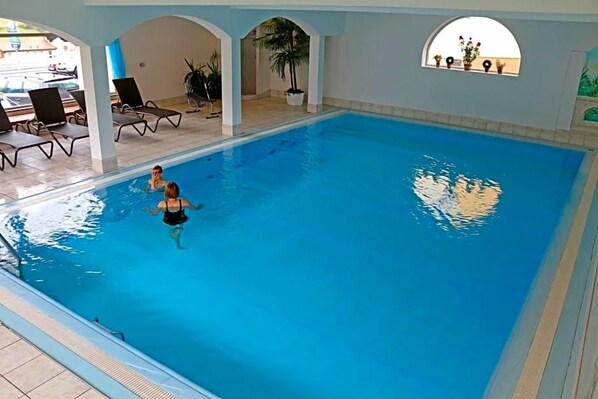 An indoor swimming pool with clear water, surrounded by lounge chairs and potted plants.