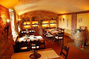 A restaurant with brick walls, wooden tables, and chairs. There are shelves with bottles and a barrel on the right.