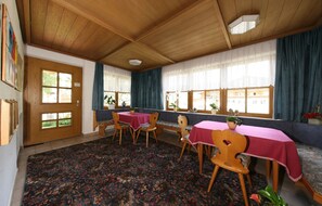 Un comedor con mesas y sillas de madera, cubiertas con manteles rojos, y una alfombra estampada.