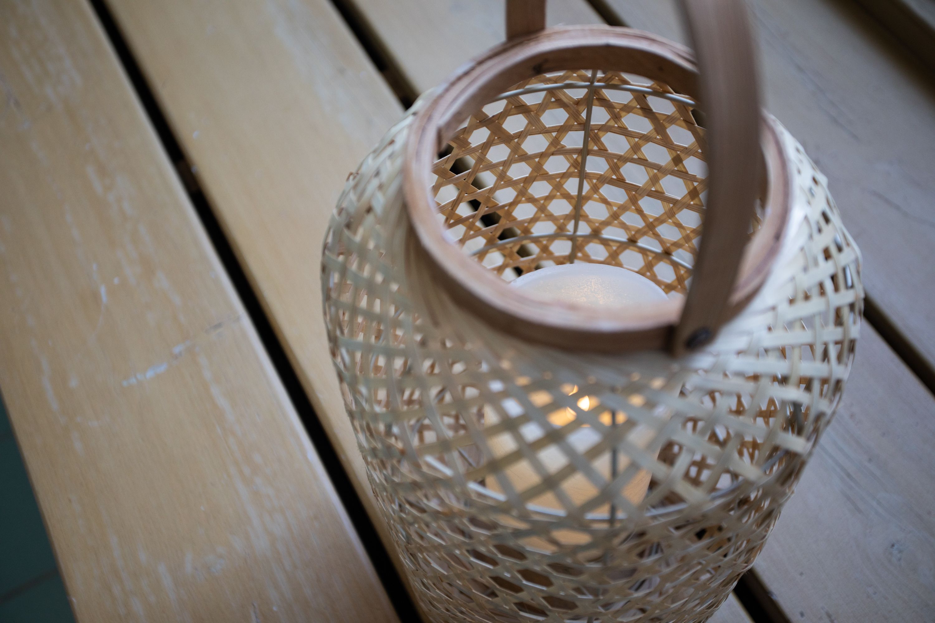 A wicker lantern with a handle, placed on a wooden surface.