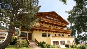 A multi-story building with a sign reading "Pension Tirol." It features a wooden balcony on the upper floor, a staircase leading to the entrance, and a well-maintained lawn in front. - Pension Tirol (Nauders)