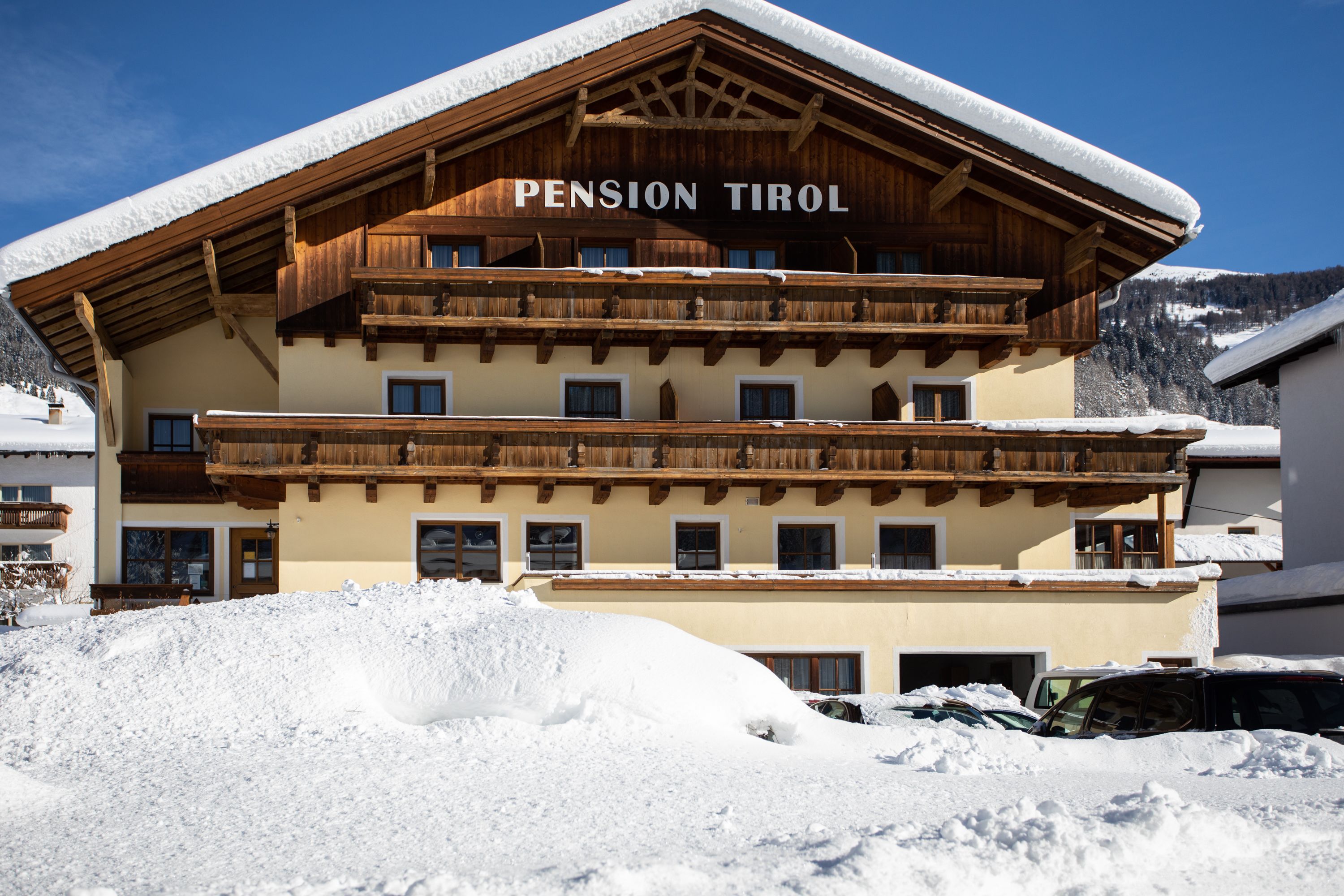 A multi-story building named "Pension Tirol" with a wooden facade and balconies, surrounded by snow.