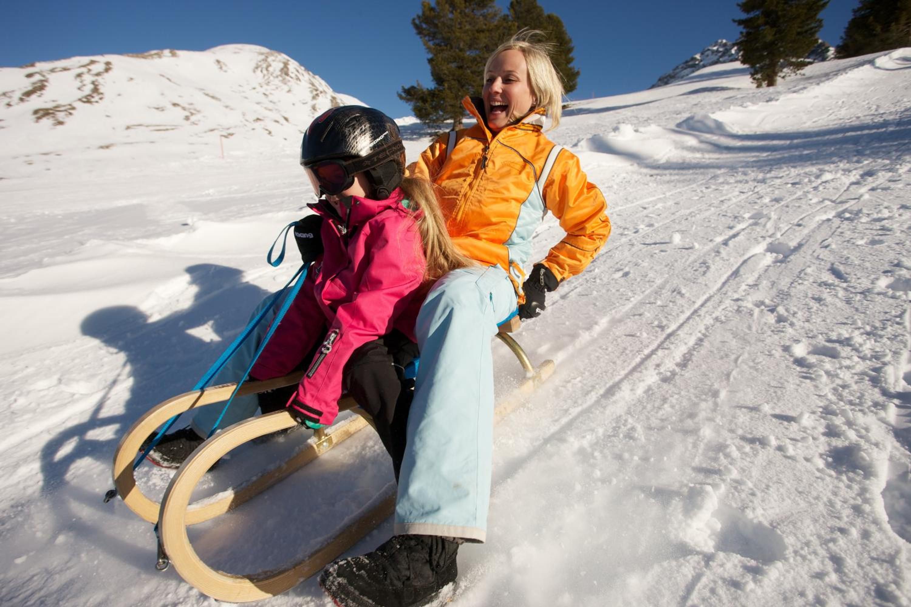 Deux personnes dévalent une pente enneigée en luge.