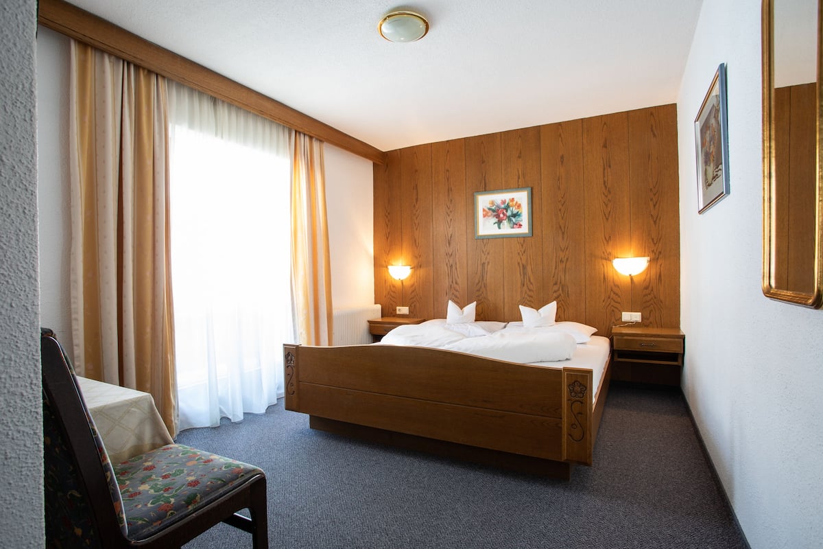 A hotel room with a wooden bed, a chair, a nightstand, and a wall-mounted lamp.