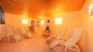 A sunlit room with four striped lounge chairs, a small table with a vase, and wall-mounted lights. - Pension Tirol (Nauders)