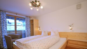 Un dormitorio con cama de madera, una silla, una ventana con cortinas y una lámpara en el techo.