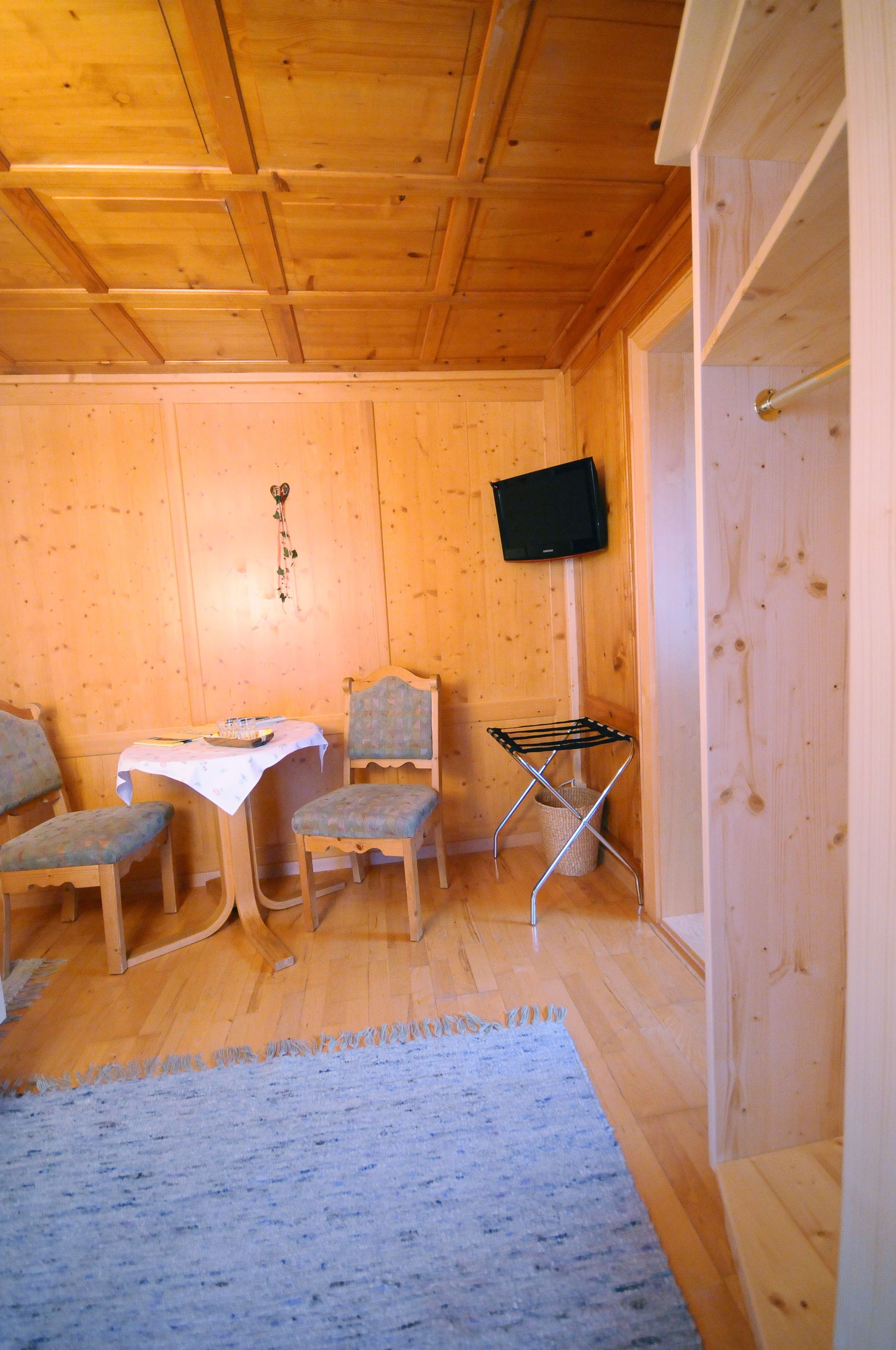L’intérieur d’une cabane en bois comprend une table à manger, deux chaises, un téléviseur fixé au mur et une petite chaise pliante.