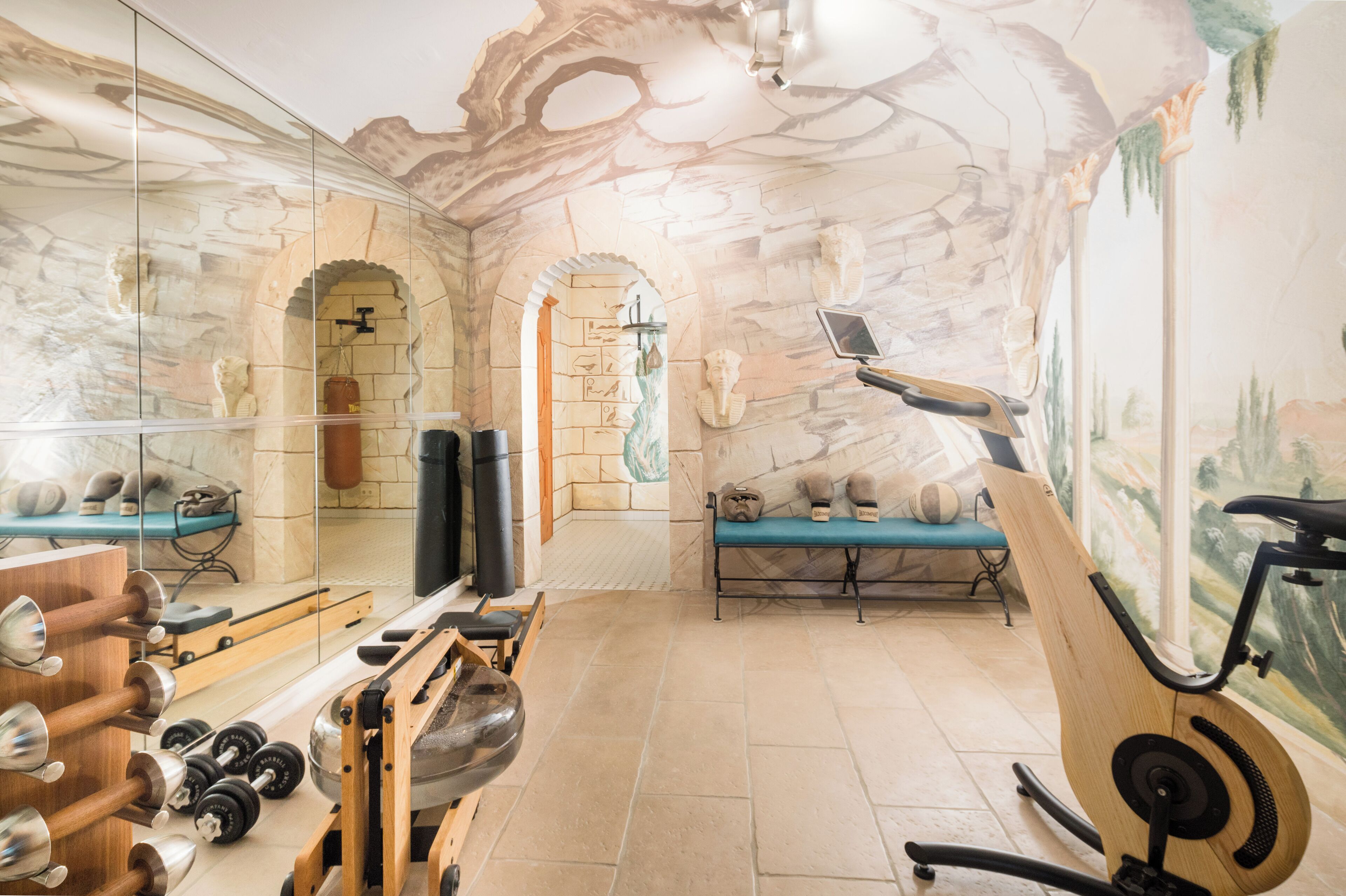 Ein Fitnessraum mit Trainingsgeräten, einer Bank und einer Wand mit einem steinartigen Wandgemälde.