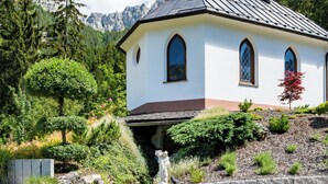 Una iglesia blanca con un campanario, rodeada de abundante vegetación y montañas al fondo.