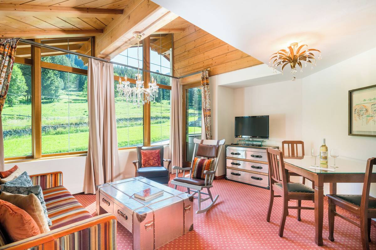 Una habitación con un ventanal grande, un televisor, una mesa de comedor con sillas, un sofá y una araña.