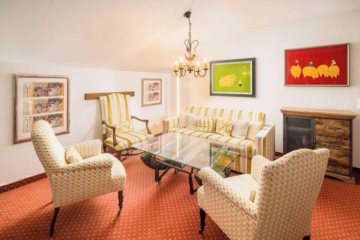 Una habitación con una mesa de centro de vidrio rodeada de sillones estampados, un sofá a rayas y una chimenea.