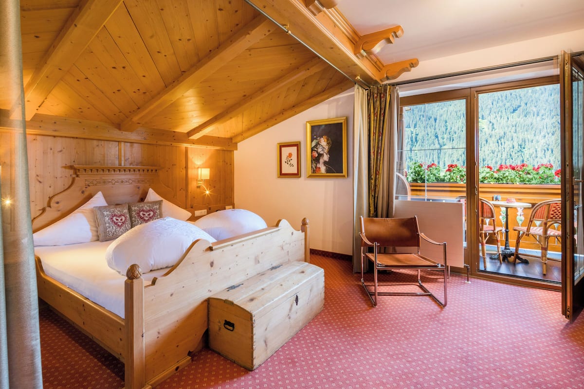 Una habitación de madera con una cama, una silla y vistas a un balcón lleno de flores.
