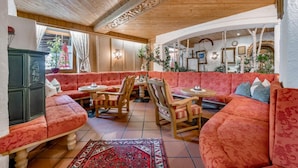 Un intérieur chaleureux avec un plafond en bois, un canapé rouge à motifs, une table à manger avec des chaises et un tapis décoratif.