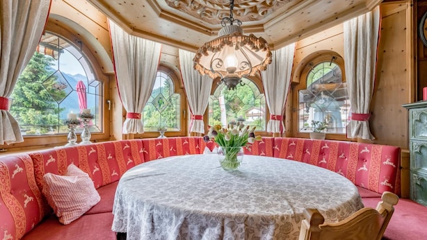 Une table ronde recouverte d’une nappe à motifs floraux, entourée de bancs rouges capitonnés ornés de motifs équestres.