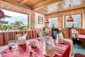 A restaurant with a mountain view, striped upholstered seating, and red tablecloths.