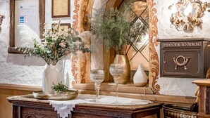 Une pièce avec un bureau en bois, un vase rempli de fleurs, un menu encadré et un meuble fixé au mur portant l’inscription « POSTKASTEN ».