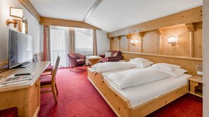 Une chambre d’hôtel avec un lit en bois, un bureau avec une télévision, une chaise et une petite table.
