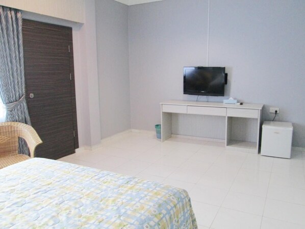 Un dormitorio con cama, escritorio, televisor y un refrigerador pequeño.