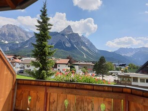 Un balcon donnant sur une chaîne de montagnes, une clôture en bois et un parterre de fleurs.