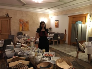 Uma sala de jantar com mesas postas para refeição, uma pessoa em pé ao centro e obras de arte nas paredes.