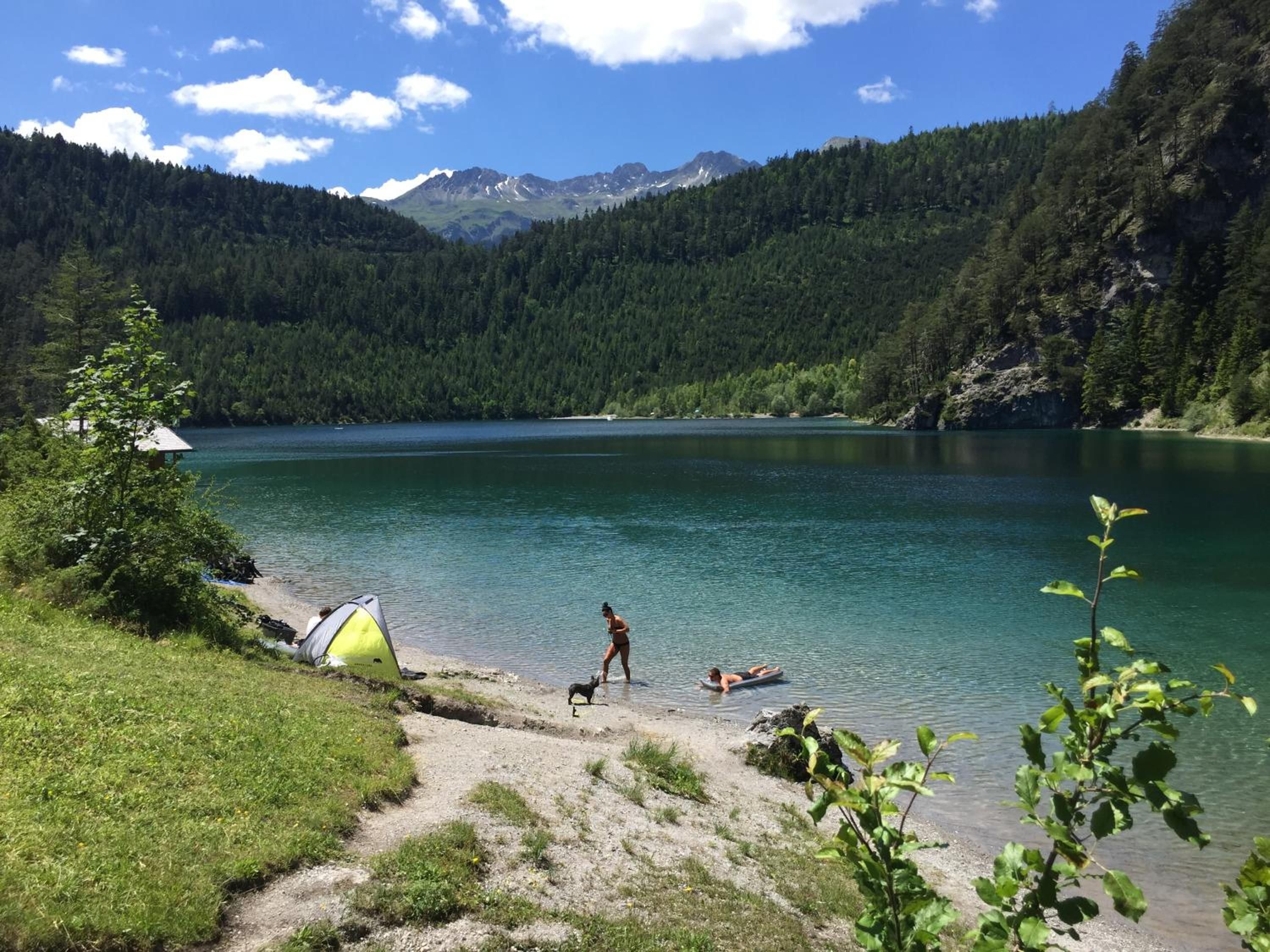 Um lago com uma tenda e uma pessoa passeando com um cachorro perto da margem.