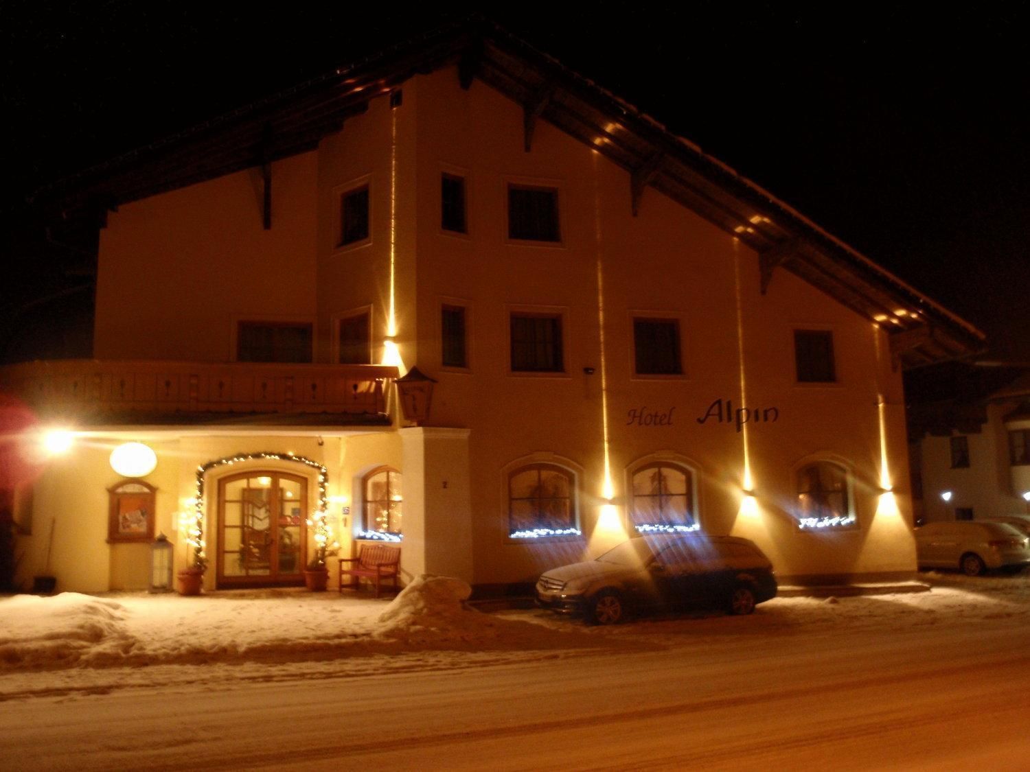 A hotel with a sign reading 'Hotel Alpeno' at night, featuring a snow-covered ground and a parked car.