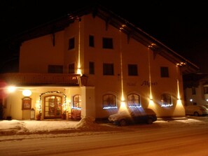 Um hotel com uma placa indicando 'Hotel Alpeno' à noite, com o chão coberto de neve e um carro estacionado.