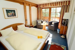 Quarto de hotel com uma cama de casal, uma mesinha com uma garrafa, uma cadeira e um sofá.