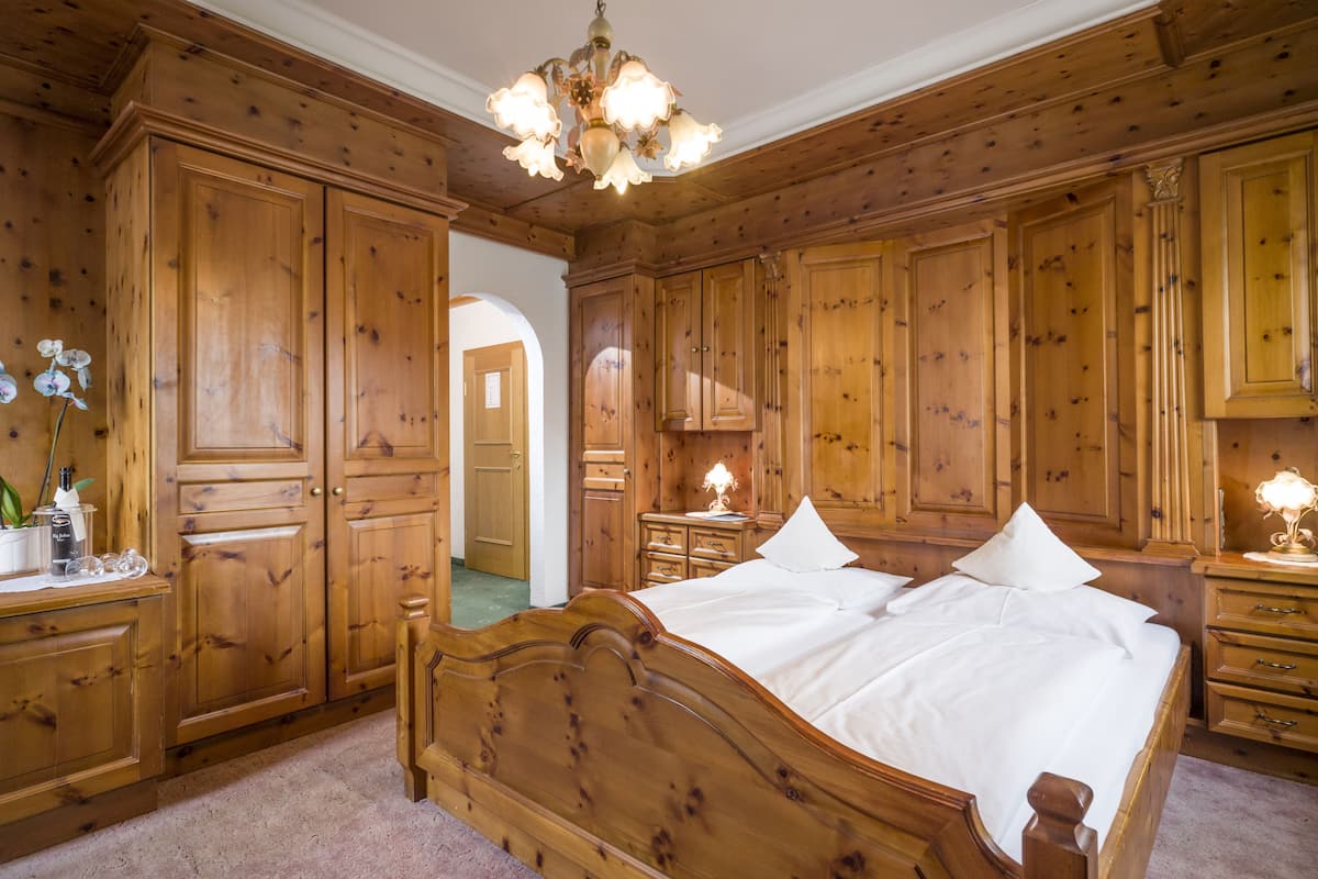 Een slaapkamer met houten lambrisering, een groot bed, een houten garderobe en een kroonluchter.
