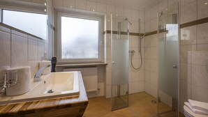A modern bathroom with a glass-enclosed shower, a large window, and a wooden vanity. - Hotel Gasthof Gradlwirt (Niederndorf)