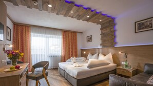 A modern hotel room with a wooden ceiling, a bed with white linens, a desk with a vase of flowers, and a sofa. - Hotel Gasthof Gradlwirt (Niederndorf)