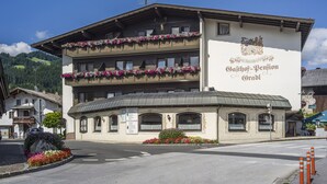 A multi-story building with balconies adorned with flowers, a sign reading "Gajthof-Pension," and a mountainous backdrop. - Hotel Gasthof Gradlwirt (Niederndorf)