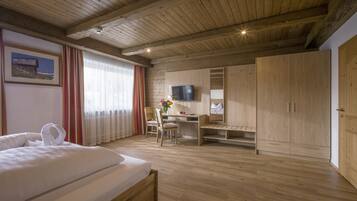 A hotel room with a wooden ceiling, a bed, a desk, a chair, a TV, and a wardrobe.
