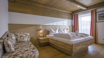 Een slaapkamer met een houten plafond, een bed met witte lakens, een bloemenbank en een nachtkastje met een fles.