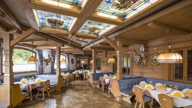 A restaurant with wooden beams, stained glass windows, and a tiled floor. Tables are set with white tablecloths and yellow fans. - Hotel Gasthof Gradlwirt (Niederndorf)