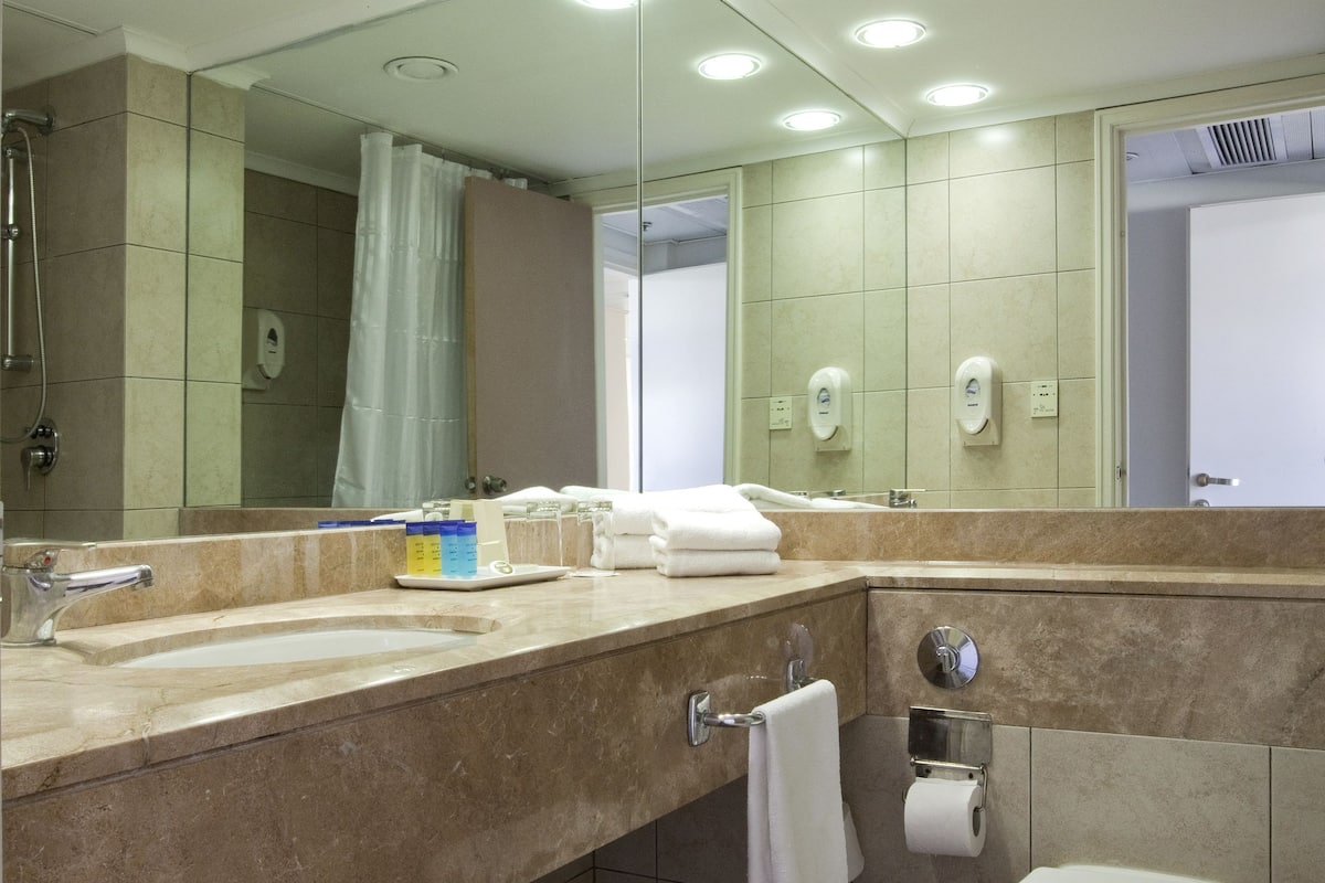 A modern bathroom with a large mirror, multiple sinks, a toilet, and a shower area.