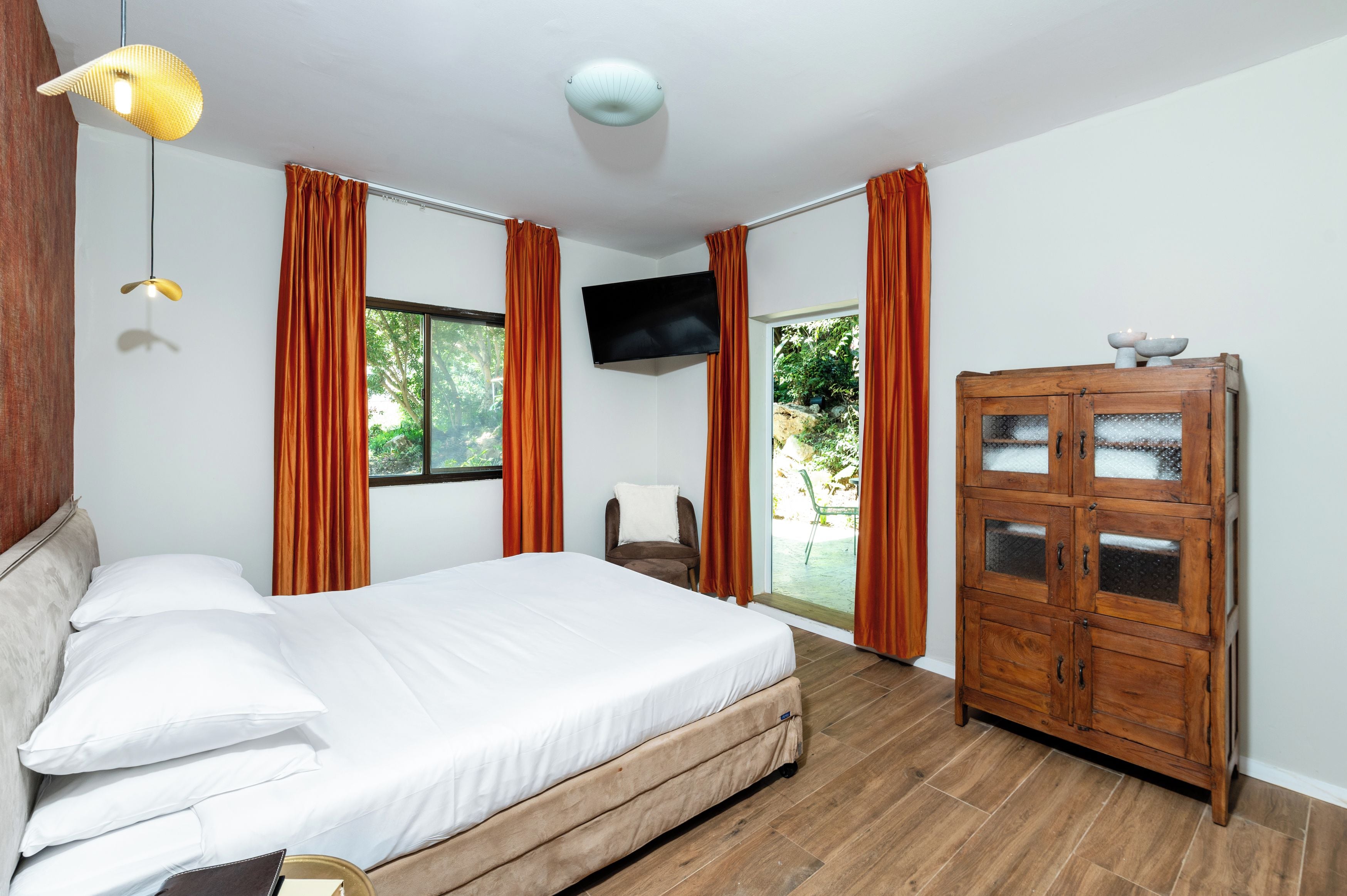 A bedroom with a bed, a television, a wooden cabinet, and a window.