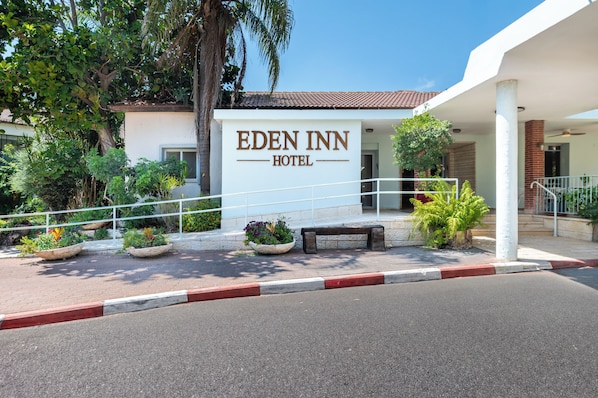 The Eden Inn Hotel entrance with a white facade, a red and white curb, and potted plants.