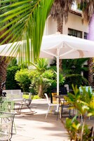 Un área de estar al aire libre con una sombrilla blanca, diferentes sillas y una palmera.