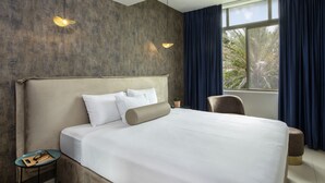 A modern hotel room with a large bed, a small table with a lamp, and a window with curtains. - Eden Inn (Zikhron Ya'aqov)