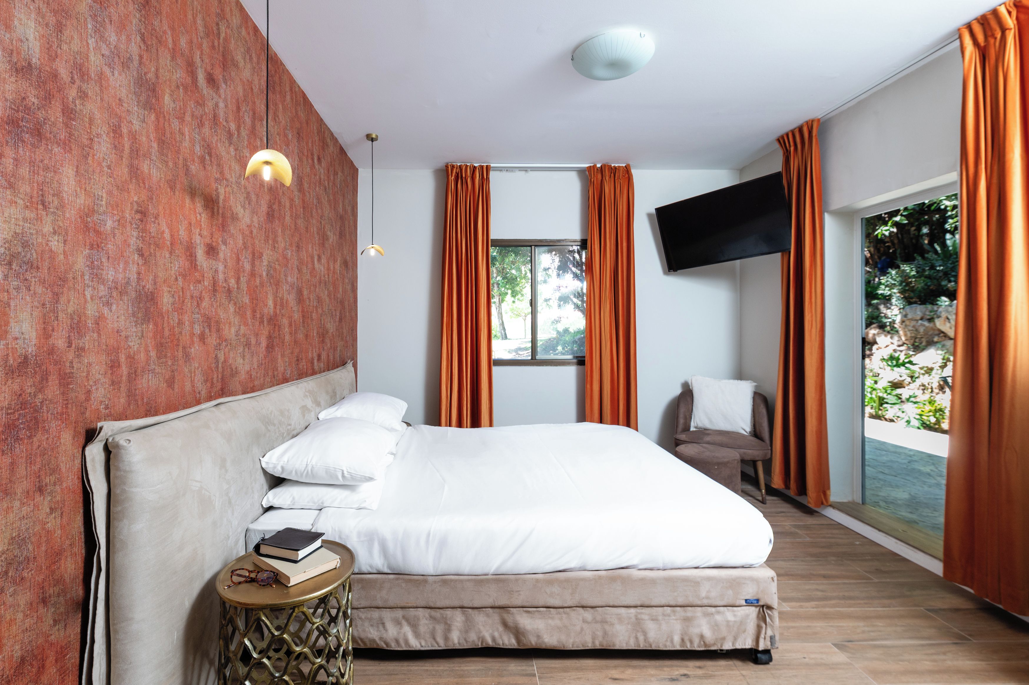 A modern bedroom with a large bed, a TV mounted on the wall, and a view of the outdoors.