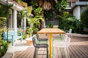 An outdoor patio with a wooden table and chairs, surrounded by lush greenery and plants.
