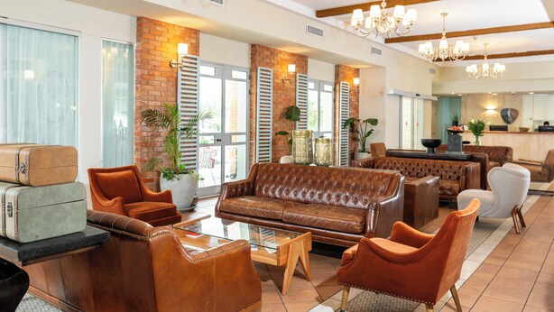 A spacious lobby with a leather sofa, armchairs, and a glass coffee table. There are potted plants and a brick wall. - Eden Inn (Zikhron Ya'aqov)