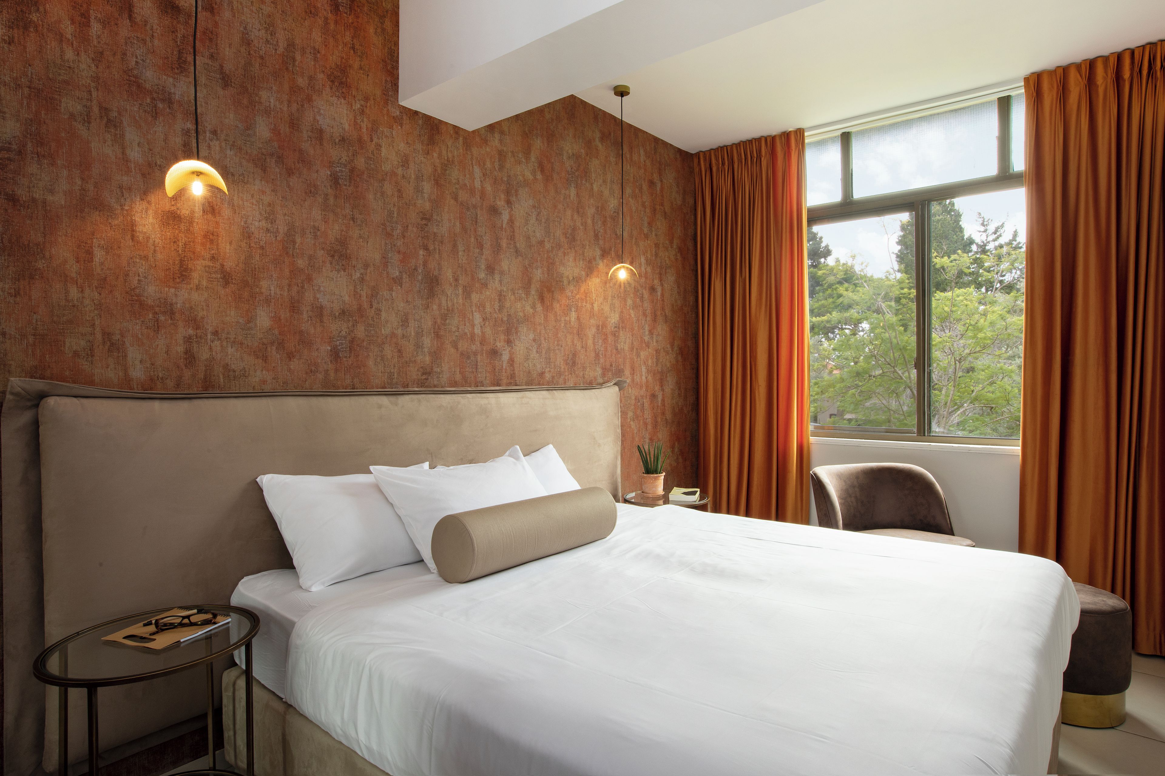A hotel room with a large bed, a bedside table, a chair, and a window with curtains.